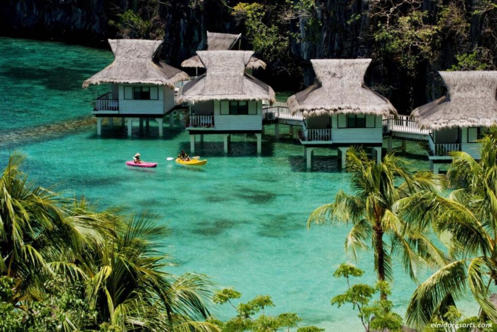 overwater bungalows situated in a large bay and guest kayaking on the calm emerald waters 