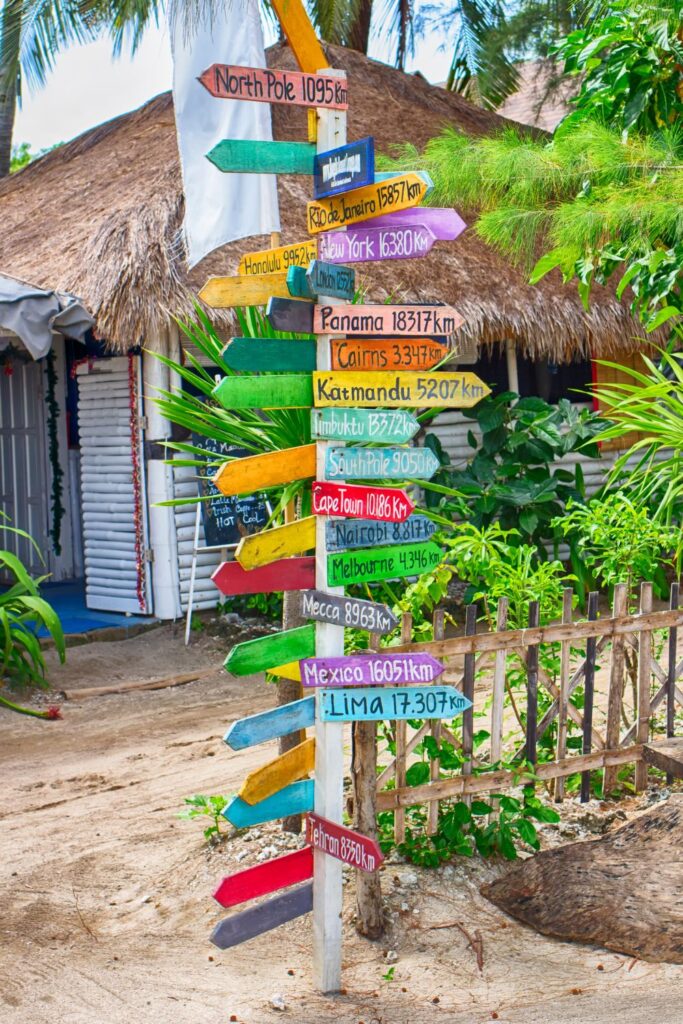 a pole with colorful signages of different locations and distance from Gili Air