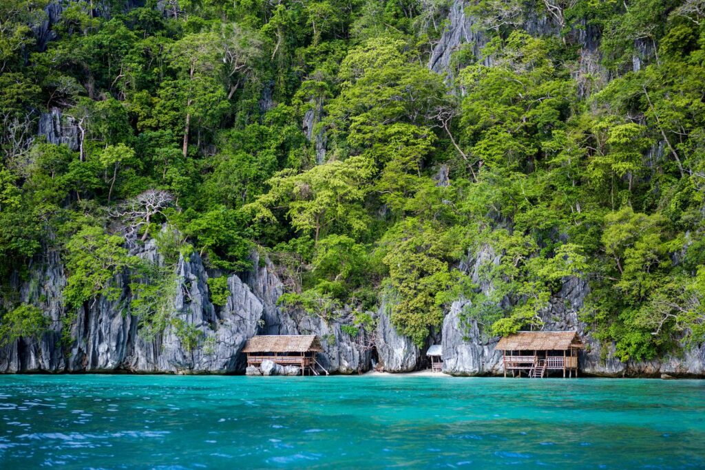 Overwater bungalows in the Philippines with forested limestone cliffs and turquoise water