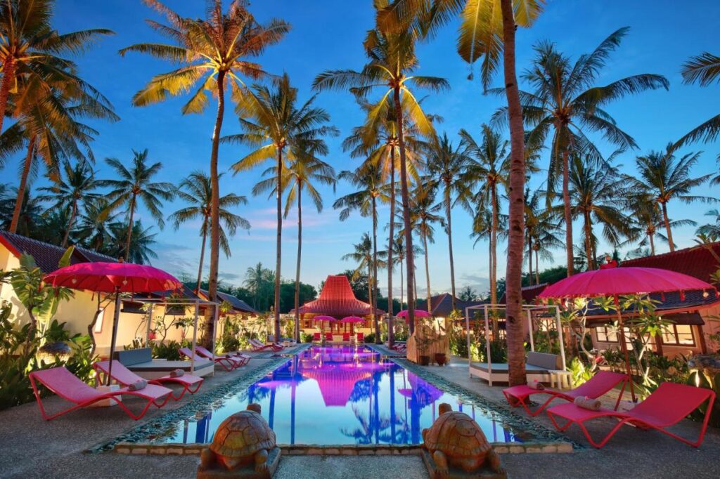 outdoor pool surrounded by palm trees and pink tropical umbrellas and pink chairs